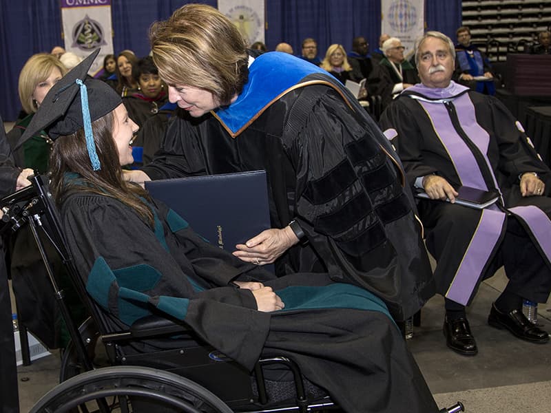 A smiling Green receives her diploma from Dr. Jessica Bailey, dean of SHRP, while other school deans look on during UMMC’s Commencement May 25.